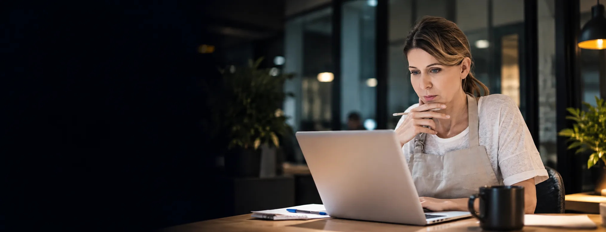 A business owner thoughtfully reviewing her laptop at her desk