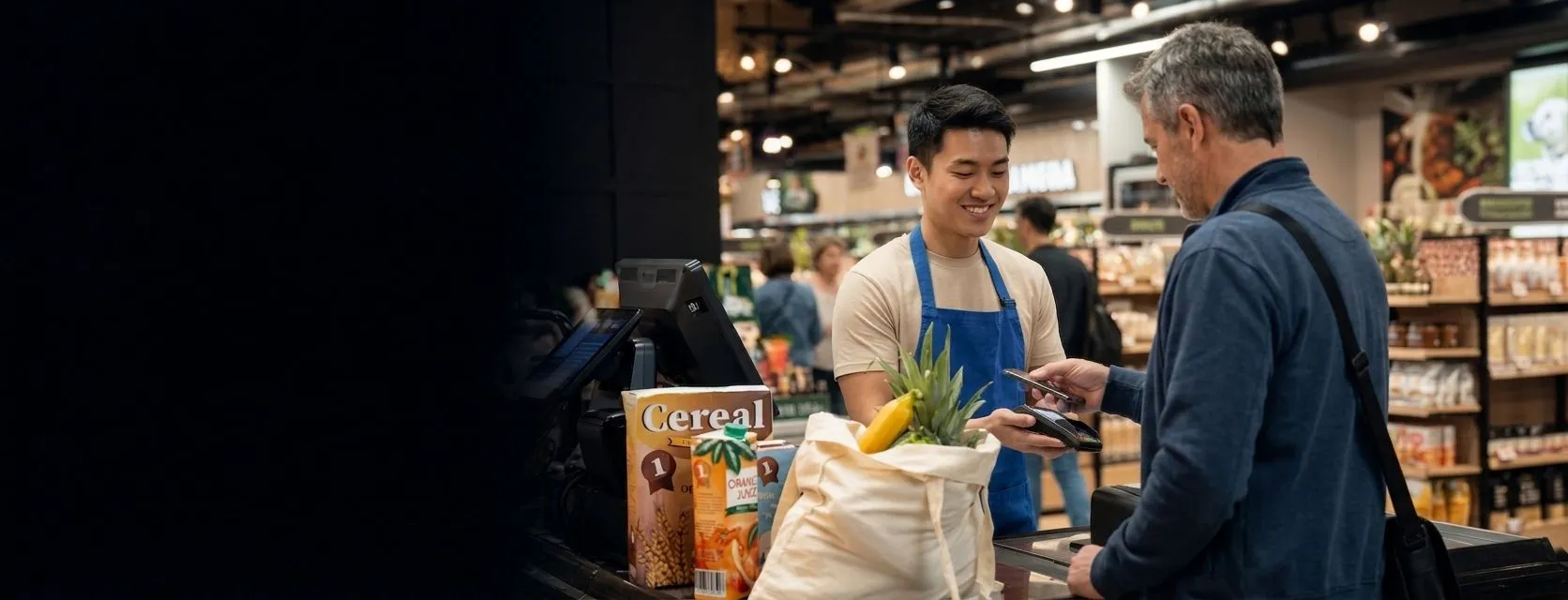 A cashier taking a contactless card payment from a customer at a supermarket checkout